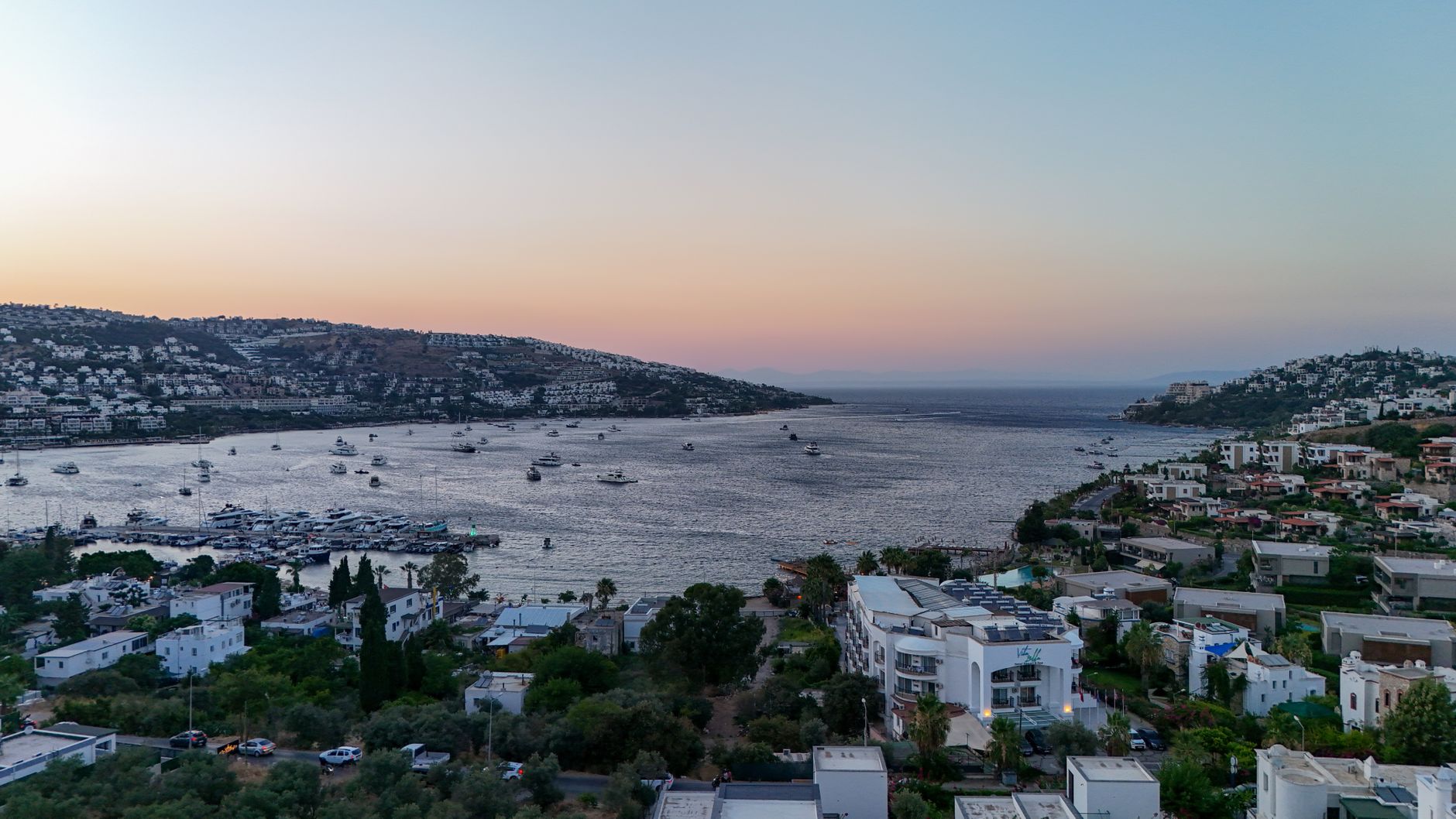 Aerial view of Bodrum Marina with yachts and vibrant sunset sky over the Aegean Sea.
