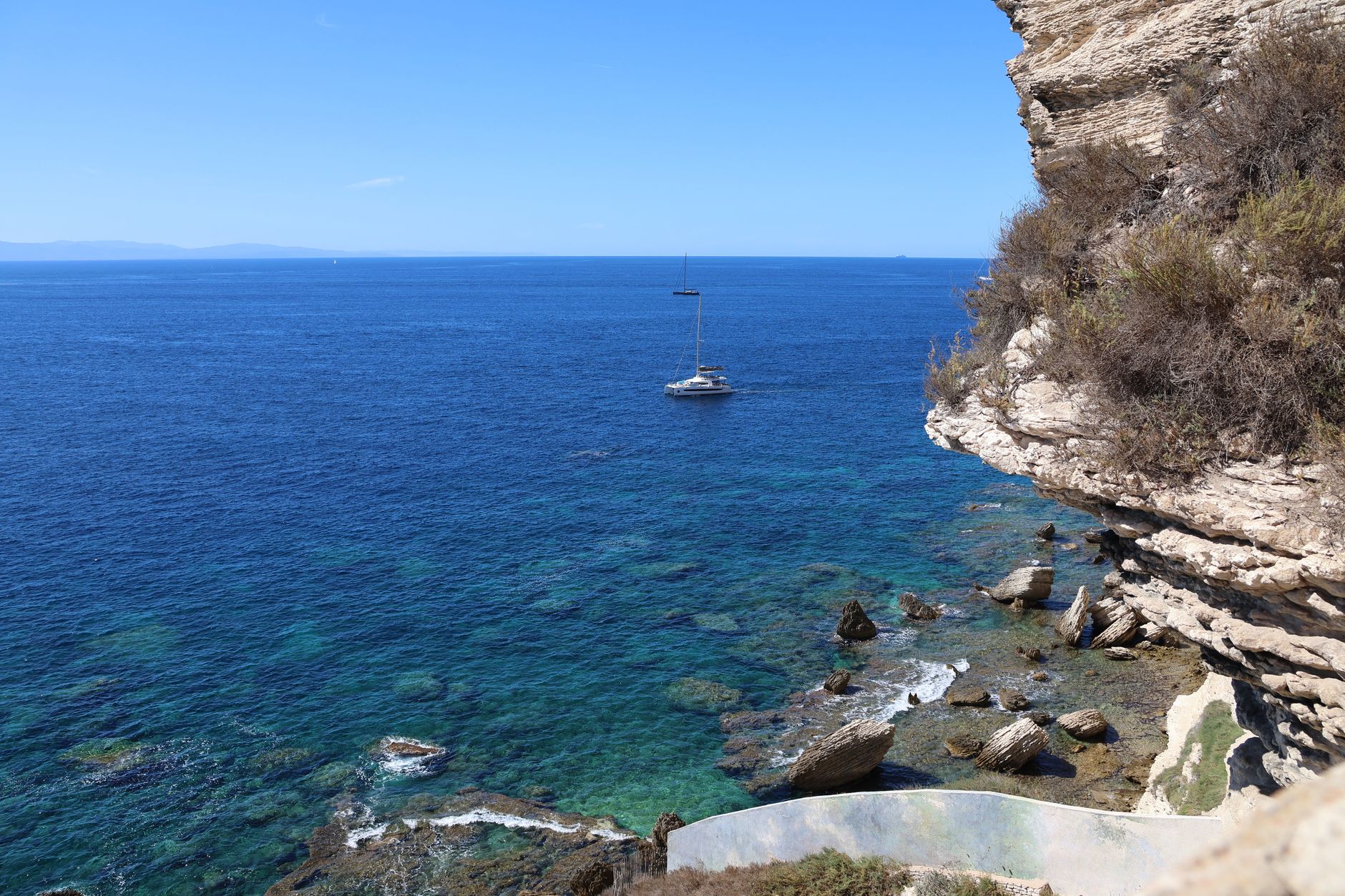 A serene view of a sailboat on the blue Mediterranean Sea near rocky cliffs.