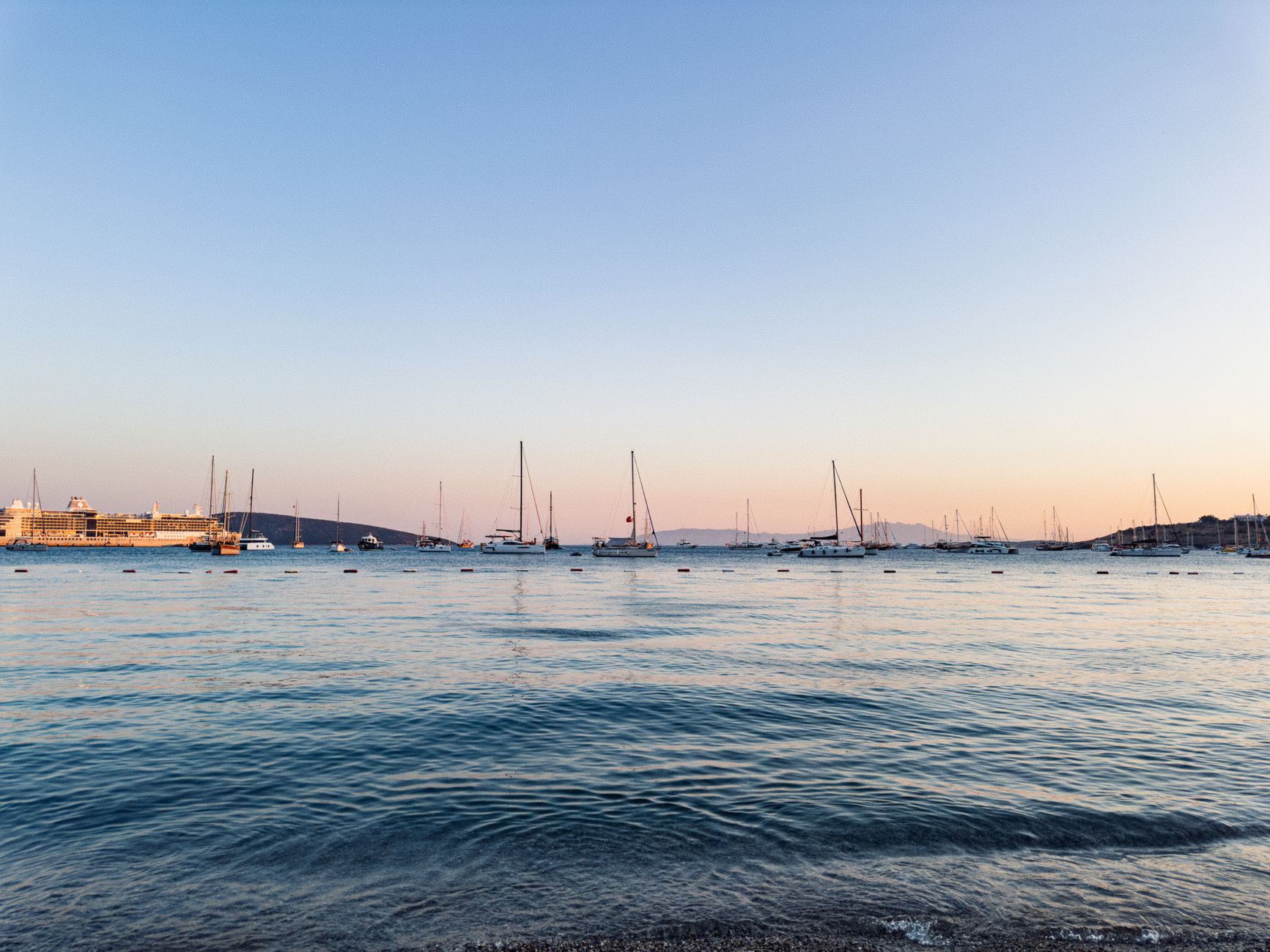 Serene view of a harbor at sunset with sailboats on calm water, ideal for travel and relaxation themes.