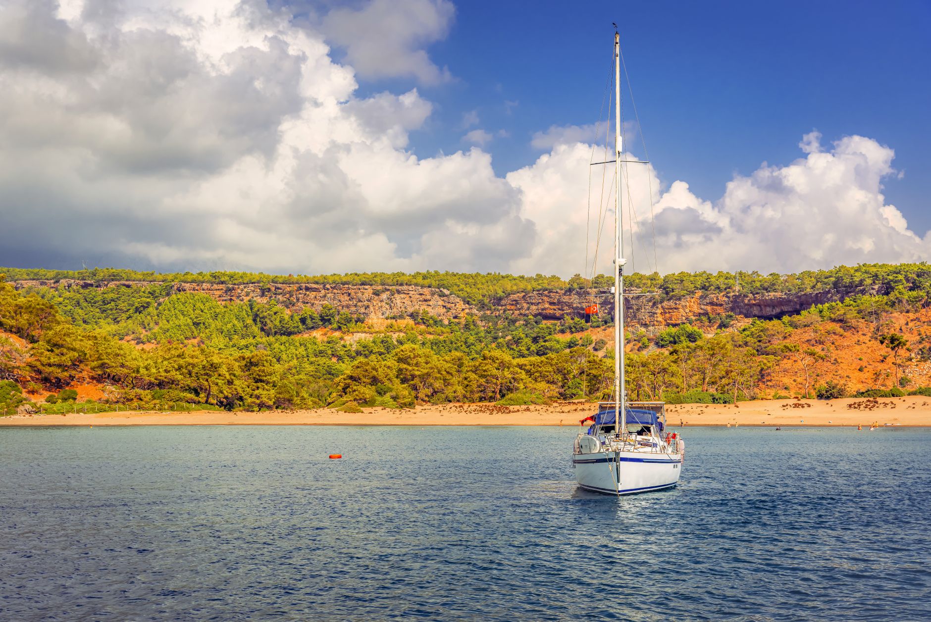 A yacht sailing near a scenic coastline with vibrant summer colors and clear skies.
