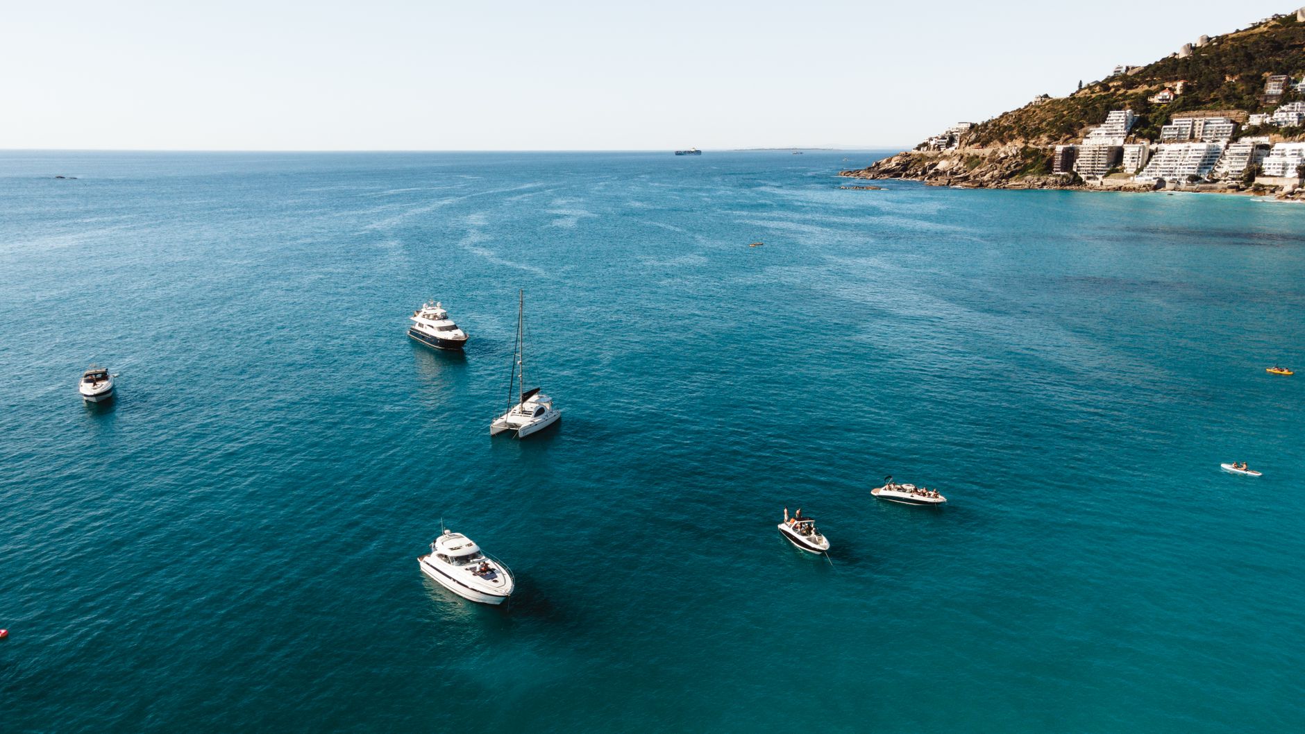 Aerial shot of luxury yachts in clear blue waters near the coast of Cape Town.