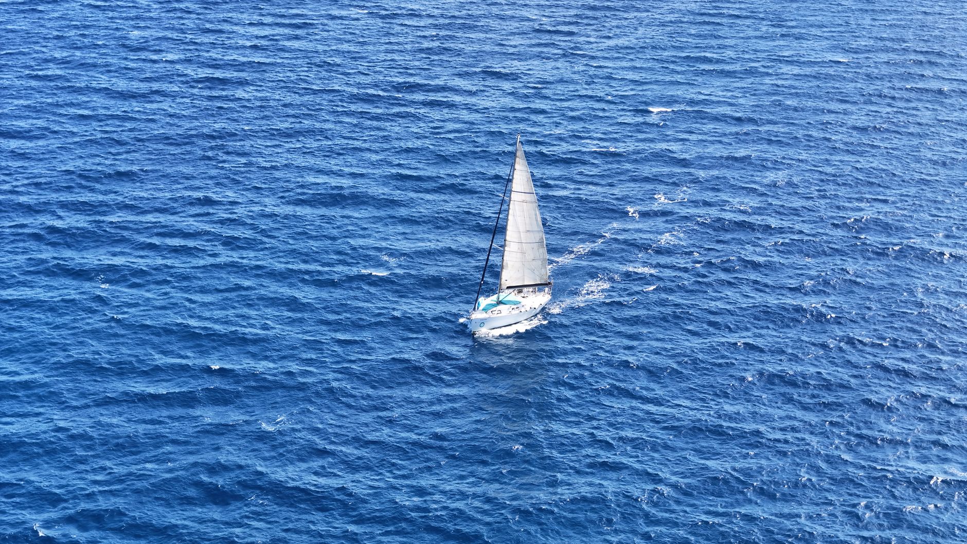 A lone sailboat gliding over deep blue waters off the coast of Spain in the Mediterranean Sea.