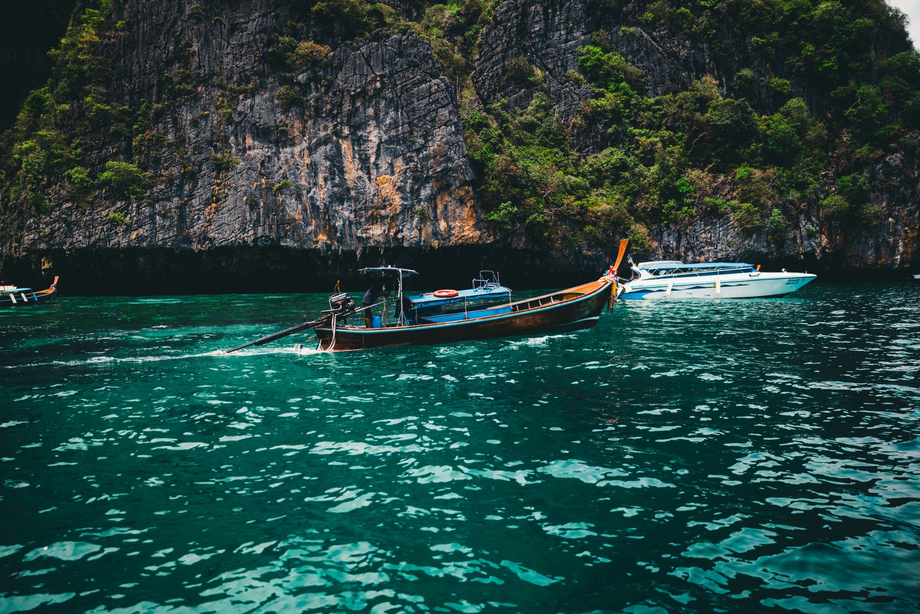 Longtail boat glides in the turquoise sea against stunning limestone cliffs in Phuket, Thailand.
